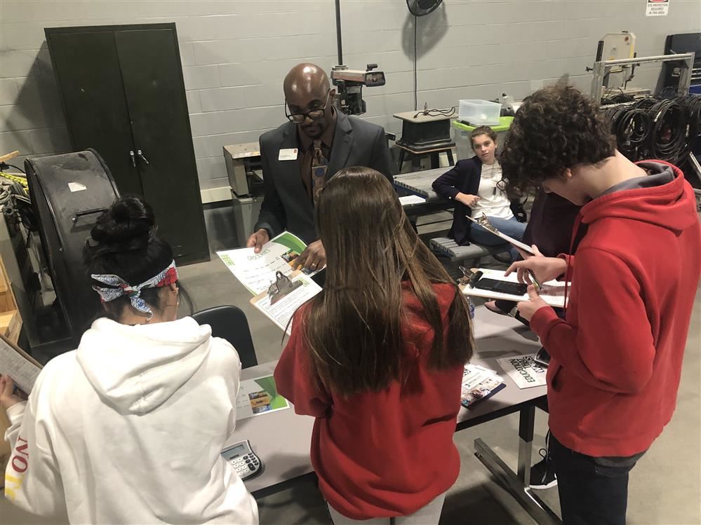 Three students participating in Reality Check, speaking with community volunteer.